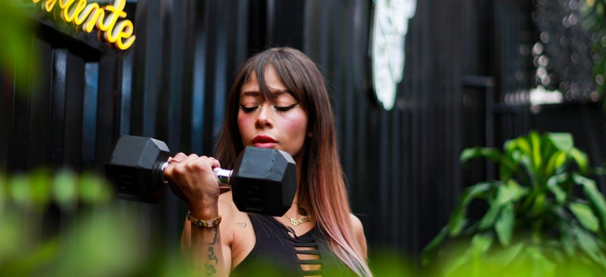 Fitness woman with long hair lifting a dumbbell outdoors, focusing on her strength training.