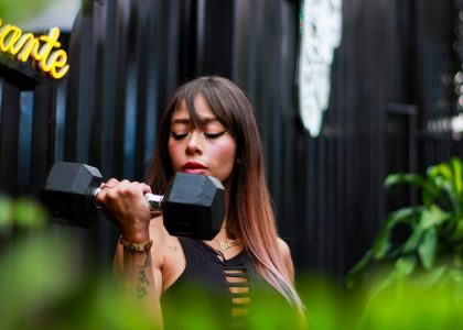 Fitness woman with long hair lifting a dumbbell outdoors, focusing on her strength training.