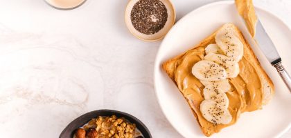 Flat lay of a nutritious breakfast featuring banana toast, chia seeds, and nuts on a marble surface.