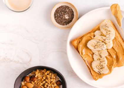 Flat lay of a nutritious breakfast featuring banana toast, chia seeds, and nuts on a marble surface.